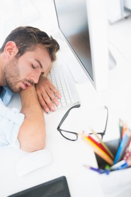 Side view of a male artist with head resting on keyboard in the office